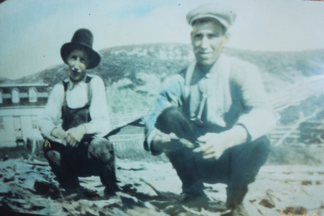Jack Hann on his Big Fish Flake, Merasheen in 1925 and his son Tom Hann to his right. You can see the family house in the middle of the meadow and it was later moved to the right under the shelter of the hill.